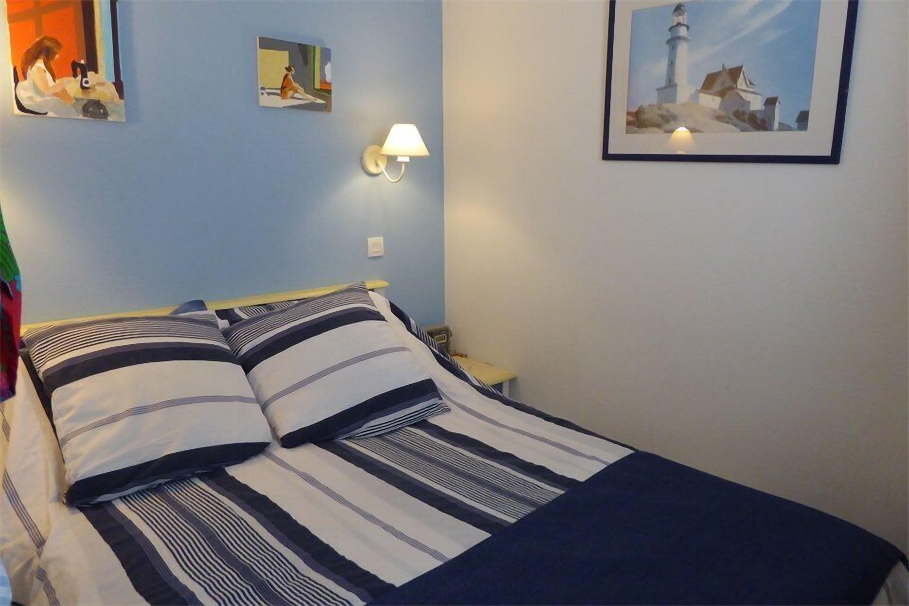A bed with striped bedding, a nightstand with a lamp, and a framed picture of a lighthouse on the wall.
