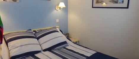 A bed with striped bedding, a nightstand with a lamp, and a framed picture of a lighthouse on the wall.