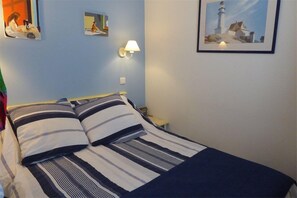 Ein Bett mit gestreifter Bettwäsche, ein Nachttisch mit Lampe und ein gerahmtes Bild eines Leuchtturms an der Wand.