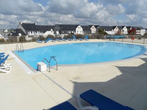 Ein Schwimmbecken mit blauem Wasser, umgeben von Liegestühlen und einem Zaun.