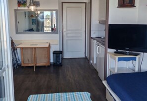 A compact room with a bed, a television, a small kitchenette, and a door leading to another room. - Appartement pour 4 avec vue port et piscine (ARZON)