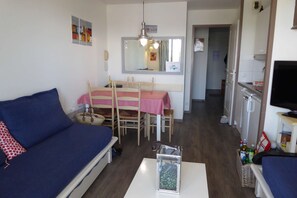 Ein kompakter Wohnbereich mit Sofa, Esstisch, Stühlen, Fernseher und Küchenzeile.
