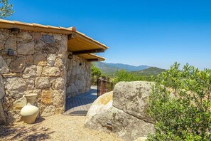 Ein Steinhaus mit Holzdach, einem gepflasterten Eingang und einem großen Felsen im Vordergrund.