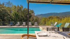 Uma área de refeições à beira da piscina, com uma mesa posta para dois, com vista para uma piscina e uma paisagem montanhosa.