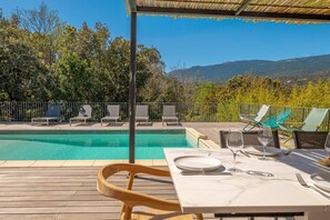 Ein Essbereich am Pool mit einem Tisch für zwei Personen mit Blick auf einen Swimmingpool und eine gebirgige Landschaft.