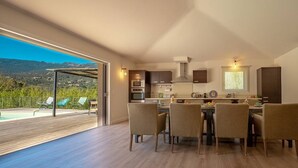Uma cozinha moderna com área de refeições, janelas amplas e vista para uma piscina e montanhas.