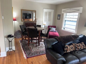 A living room with a leather sofa, a dining table with chairs, a TV, and a window with blinds. - Charming 2-bedroom apartment with AC in vibrant Denver (Denver)