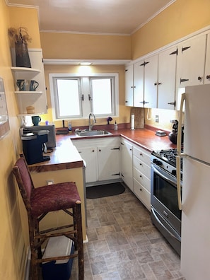 A compact kitchen with white cabinets, a sink, a stove, and a chair. - Charming 2-bedroom apartment with AC in vibrant Denver (Denver)