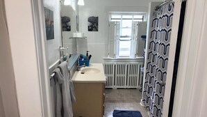 Een badkamer met een wastafel, spiegel, handdoekhouder, douchegordijn en een raam.