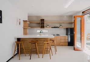 A modern kitchen with a white countertop, wooden stools, and built-in shelves.