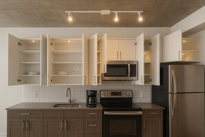 Een moderne keuken met open kastjes, een magnetron, een koelkast, een koffiezetapparaat en een fornuis.