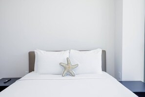 Ein Bett mit weißer Bettwäsche, einem Kissen in Form eines Seesterns und einer Fernbedienung auf dem Nachttisch.