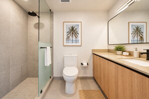 A modern bathroom with a glass shower enclosure, a toilet, a sink with a wooden vanity, and framed artwork on the wall. - LUXURY 1BR/1BA DOWNTOWN APARTMENT (Miami)