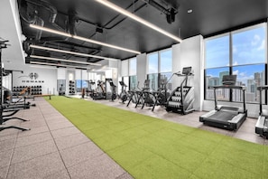 A modern gym with exercise equipment, a green turf area, and large windows offering a city view. - LUXURY 1BR/1BA DOWNTOWN APARTMENT (Miami)