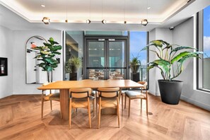 A modern dining area with a wooden table and chairs, large windows, and potted plants. - LUXURY 1BR/1BA DOWNTOWN APARTMENT (Miami)