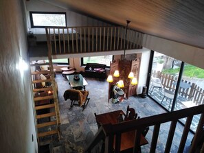Ein Loft-Zimmer mit hoher Decke, einer Holztreppe, einem Essbereich mit Glastisch und Blick ins Freie.