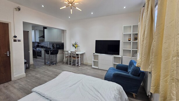 A modern hotel room with a bed, a TV, a desk with a chair, a kitchenette, and a bathroom. - Stylish Brick Lane Studio Near Tube & Dining Hub! (London)
