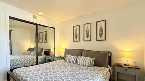 Ein Schlafzimmer mit einem großen Bett, Nachttischen, einem Spiegel und gerahmten Kunstwerken an der Wand.