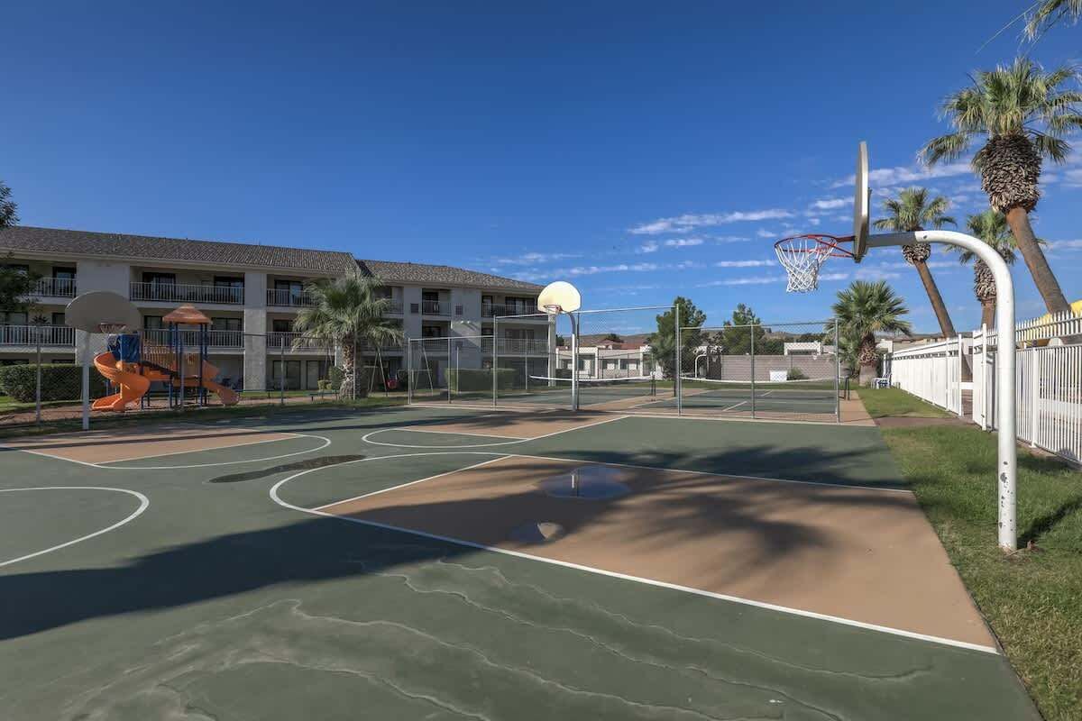 An outdoor basketball court with a net, adjacent to a building with multiple balconies.