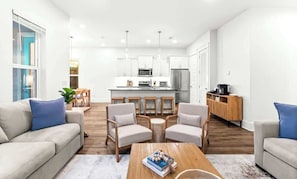 Ein modernes Wohnzimmer mit einer Couch, Sesseln, einem Couchtisch und einer Küche im Hintergrund.