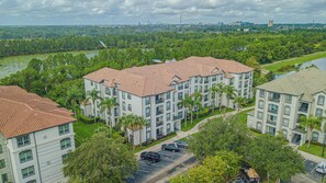 A multi-story residential building with a red-tiled roof, surrounded by lush greenery and a body of water. - Modern 3BR VistaCay Apartment Near Disney, Universal & Orlando Attractions Sleeps 7 (Orlando)