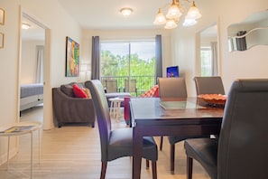 A dining area with a wooden table, chairs, and a view of greenery outside. - Modern 3BR VistaCay Apartment Near Disney, Universal & Orlando Attractions Sleeps 7 (Orlando)
