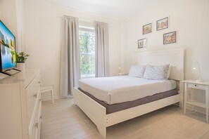 Ein Schlafzimmer mit einem Bett, einem Nachttisch, einem Fernseher und einem Fenster mit Vorhängen.
