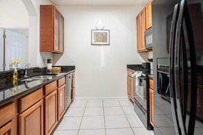 A modern kitchen with wooden cabinets, a stainless steel refrigerator, and a microwave. - Modern 3BR VistaCay Apartment Near Disney, Universal & Orlando Attractions Sleeps 7 (Orlando)