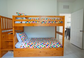 A bunk bed with a colorful checkered bedspread and pillows, a wooden headboard, and a lower bunk with a storage shelf. - Modern 3BR VistaCay Apartment Near Disney, Universal & Orlando Attractions Sleeps 7 (Orlando)