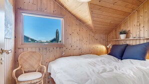 Habitación de cabaña de madera con cama, una silla de mimbre, ventana con vistas y estante con una planta.
