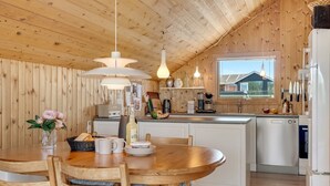 Interior de madera con una mesa de comedor, sillas, zona de cocina y una ventana con vistas.