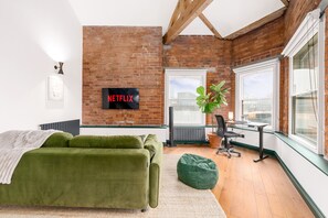 A room with a green sofa, a desk, a chair, a potted plant, and a large window. - Spacious 2BR • Pool Table • Workspace • City Centre (Manchester)