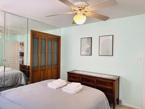 A bedroom with a bed, a dresser, a mirror, and a ceiling fan.