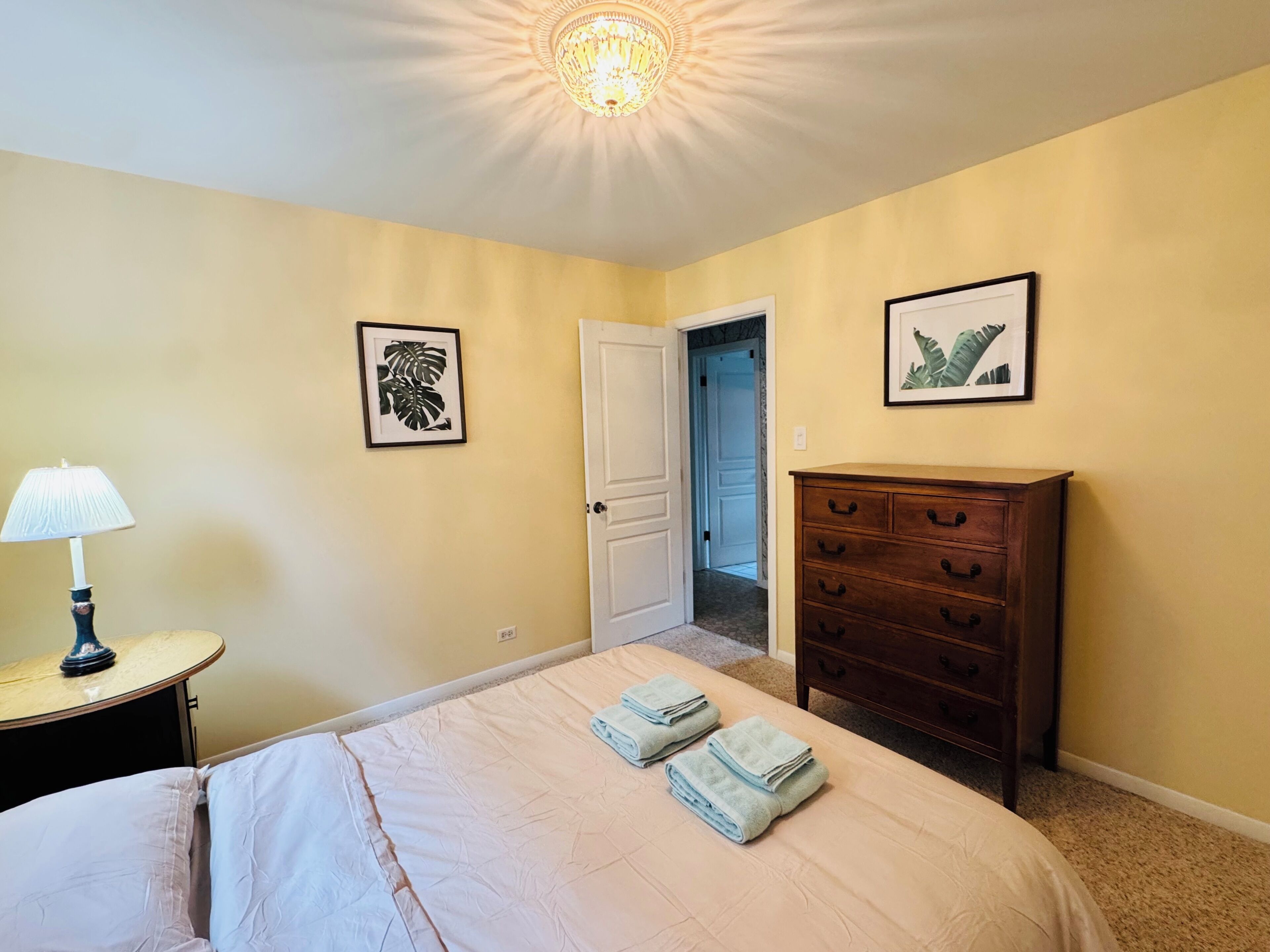 Un dormitorio con cama, cómoda, lámpara y dos cuadros en la pared.