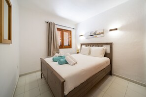 Ein Schlafzimmer mit einem Bett, einem Fenster mit Jalousien, einer Wand-Klimaanlage und einem Nachttisch mit Lampe.