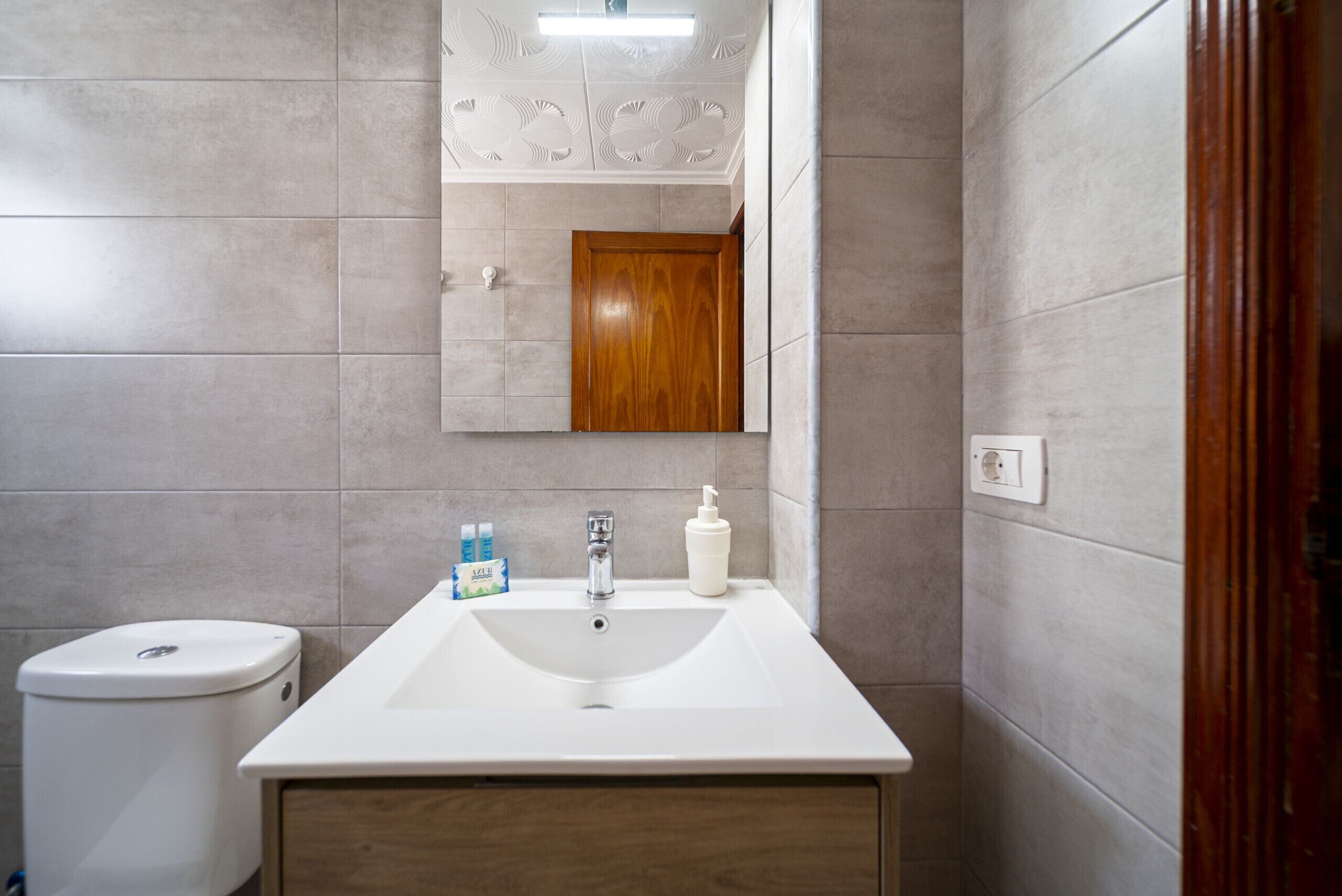 A bathroom with a white sink, a wooden door, and a mirror with a decorative ceiling.