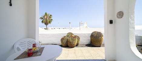 Ein Zimmer mit einem weißen Tisch, einem Stuhl, Blick auf den Strand und zwei großen Kakteen.
