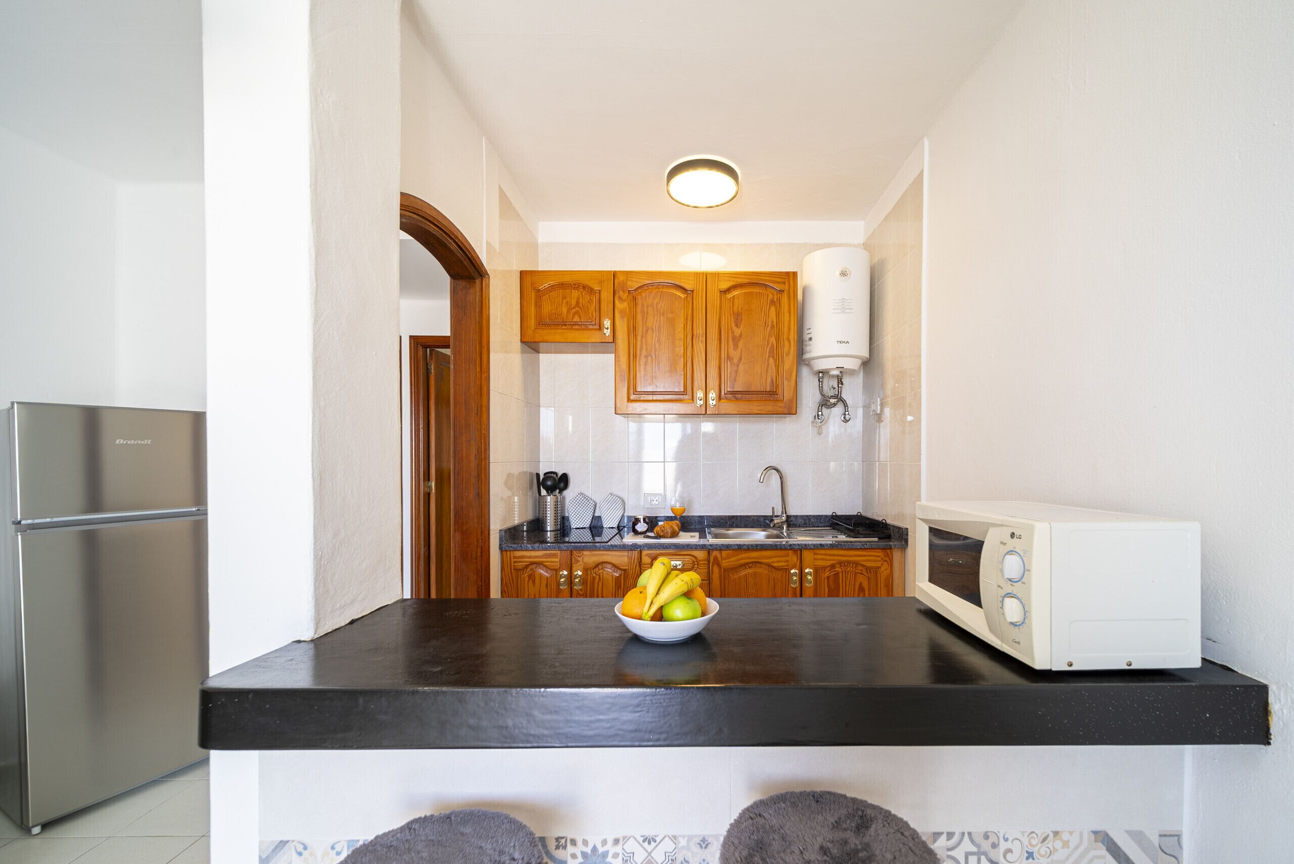 Una cocina con armarios de madera, un refrigerador de acero inoxidable, un microondas y un tazón de fruta en la encimera.