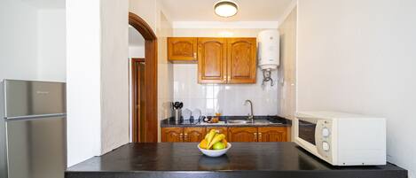 Una cocina con armarios de madera, un refrigerador de acero inoxidable, un microondas y un tazón de fruta en la encimera.