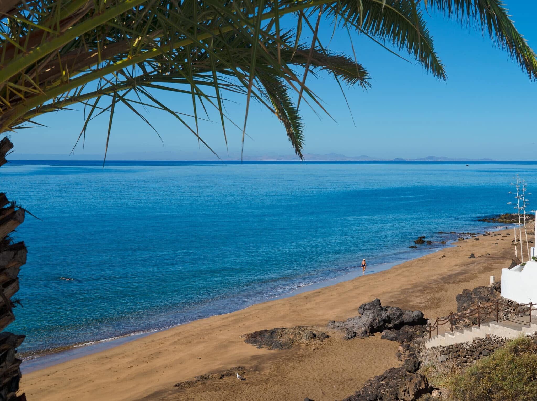 Ein Strand mit klarem, blauem Wasser, einem sandigen Ufer und einem Felsen.