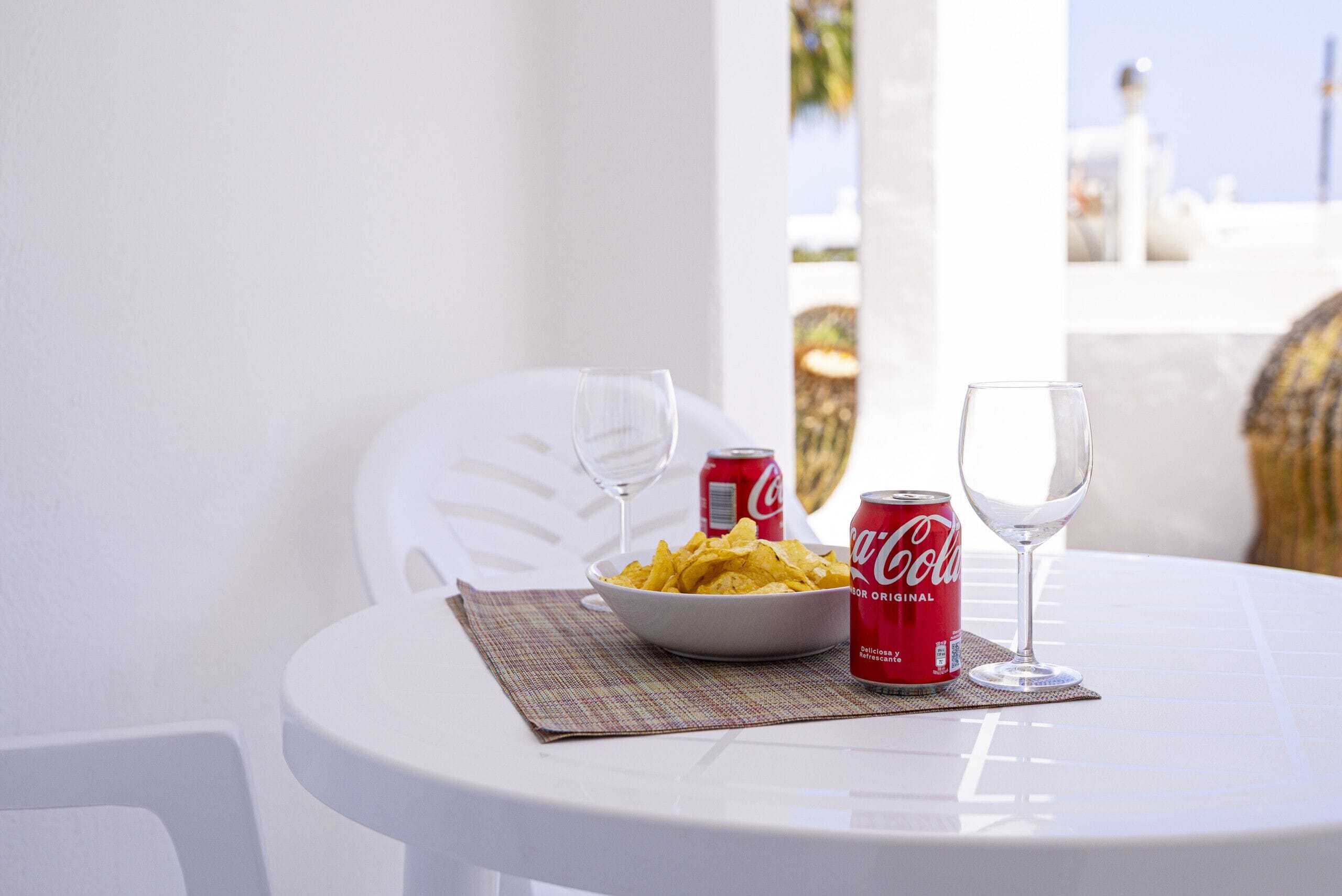 Un tavolo bianco con una ciotola di patatine, due lattine di Coca-Cola e due bicchieri da vino.
