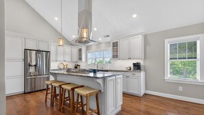 Una cocina con armarios blancos, un refrigerador de acero inoxidable, taburetes de bar de madera y una isla grande.