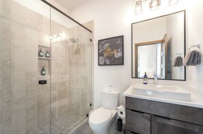 A modern bathroom with a glass shower enclosure, a toilet, a sink with a mirror, and a motivational quote on the wall. - Modern Whitefish Loft | Sleeps 6 | Downtown Whitefish, Mountain Adventure Awaits (Whitefish)