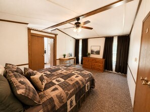 A bedroom with a bed, a dresser, a desk, a ceiling fan, and a door.