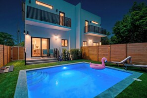 Ein modernes, zweistöckiges Haus mit Swimmingpool, Holzzaun und einem Flamingo-Schwimmpflege.