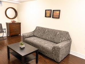 A living room with a sofa, a coffee table with a plant, a wooden dresser, and two framed pictures on the wall.