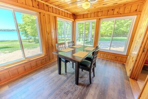 A wooden-paneled room with a table and chairs, large windows, and a view of a lake.