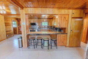 A wooden cabin interior with a kitchen, bar stools, and a trash can.