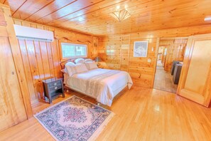 A wooden cabin interior with a bed, nightstand, air conditioning unit, and a rug.