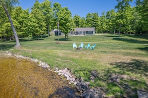 A grassy area with a small stream, a house, and three blue chairs.